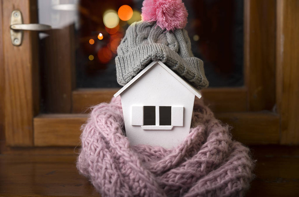house in winter - heating system concept and cold snowy weather with model of a house wearing a knitted cap - Photo, Image