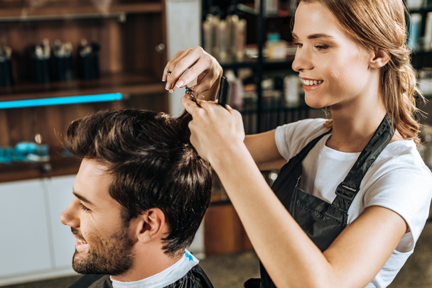 smiling young hairdresser cutting hair to handsome happy man in beauty salon - Fotoğraf, Görsel
