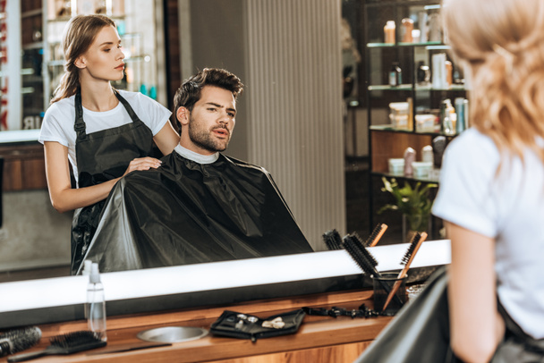 female hairstylist cutting hair to handsome young man in beauty salon - Photo, Image