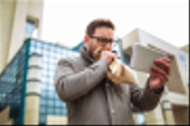 Бизнесмен держит бумажный пакет над ртом, как будто у него приступ паники и он смотрит в цифровой планшет
. - Фото, изображение