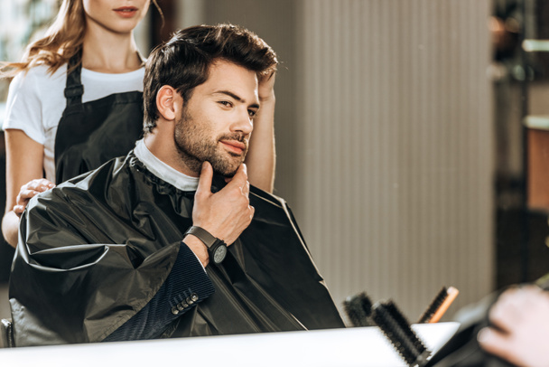 cropped shot of hairdresser doing hairstyle to handsome man looking at mirror in beauty salon - Fotó, kép