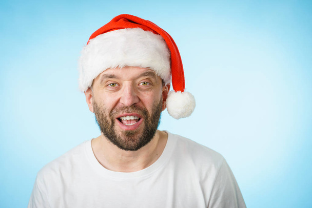 Bearded man wearing santa claus hat portrait, on blue with copy space. Christmes time. - Фото, изображение