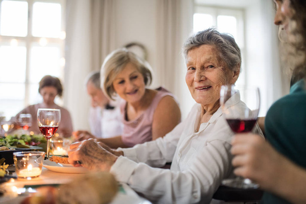 An elderly women with a family sitting at a table on a indoor family birthday party. - Foto, afbeelding