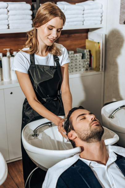 smiling female hairdresser washing hair to handsome young man in beauty salon - Fotografie, Obrázek