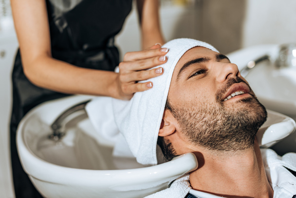 partial view of hairdresser washing hair to smiling handsome man in beauty salon  - Φωτογραφία, εικόνα