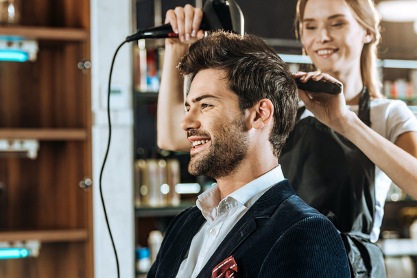 souriant jeune coiffeur séchage des cheveux à bel homme heureux dans le salon de beauté
 - Photo, image