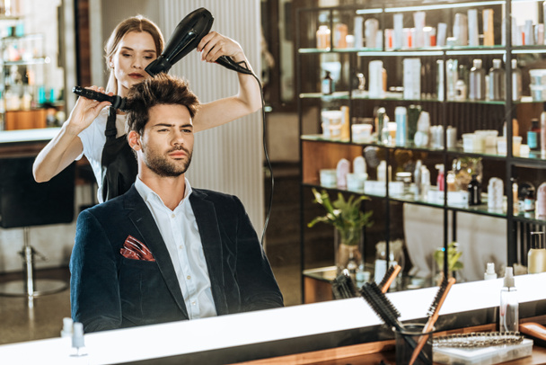 joven peluquero peinando y secando el cabello a un cliente guapo en el salón de belleza
   - Foto, imagen