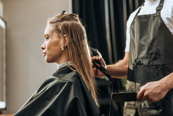 oříznuté záběr kadeřnictví drží kartáč a sušení vlasů atraktivní dívka v salonu krásy - Fotografie, Obrázek