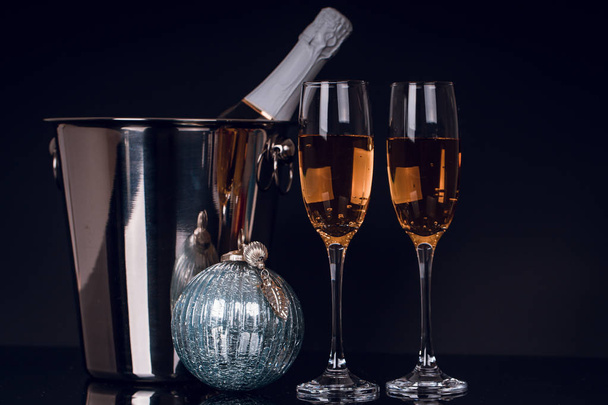 Δύο ποτήρια κρασιού με σαμπάνια, φιάλη και χριστουγεννιάτικα στολίδια πάνω σε μαύρο φόντο. Αντιγράψτε το χώρο. Καλά Χριστούγεννα και Ευτυχισμένο το νέο έτος, φόντο - Φωτογραφία, εικόνα