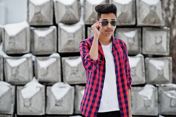 Casual young indian man in checkered shirt and sunglasses posed against stone blocks. - Zdjęcie, obraz