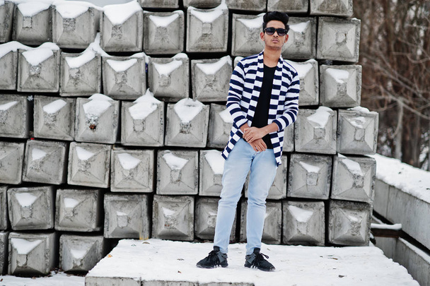 Casual young indian man in stripped sweater and sunglasses posed against stone blocks. - Zdjęcie, obraz