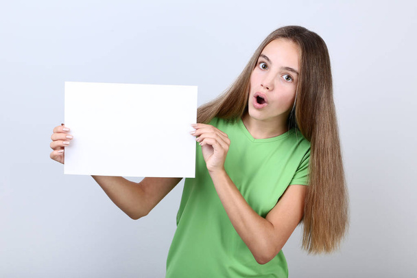 Young girl holding blank sheet of paper on grey background - Foto, Imagen