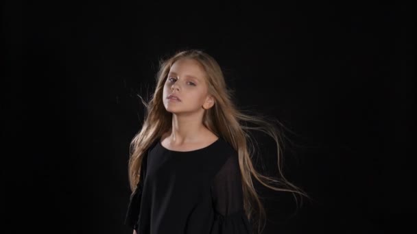 Porträt eines kleinen Modells im Studio isoliert auf schwarzem Hintergrund. Sie berührt ihre Haare in Zeitlupe, blickt in die Kamera, posiert. hd - Filmmaterial, Video