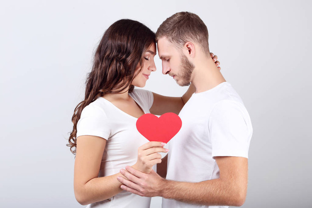Beautiful young couple holding red paper heart on grey background - Photo, image