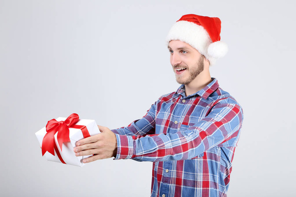 Young man in santa hat holding gift box on grey background - Photo, Image