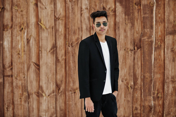 Casual young indian man in black blazer and sunglasses posed against wooden background. - Zdjęcie, obraz