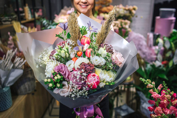 Nice and colorful bouqette of different flowers. Female florist hold it and smile. She is in flower shop. Cut view. Close up. - Photo, image