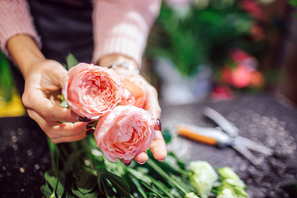Close up of beautiful orange with pink roses woman hold in hand. Scissors and green plants are behind flowers. - Valokuva, kuva