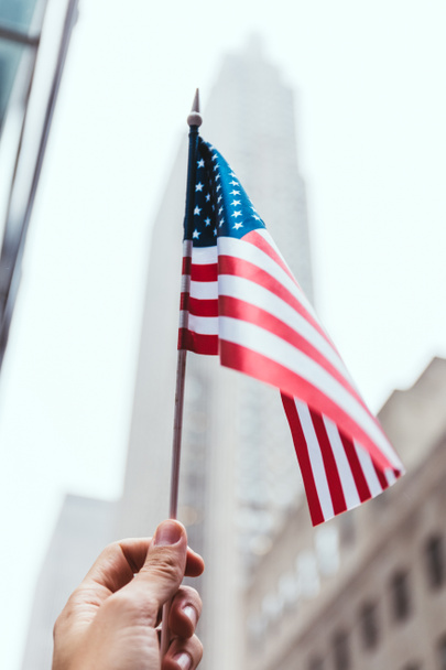abgeschnittene Aufnahme eines Mannes mit amerikanischer Flagge in der Hand und verschwommener New Yorker Straße im Hintergrund - Foto, Bild