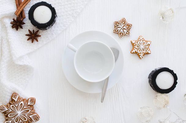 Christmas background. Empty white cup, gingerbread, candles and knitted scarf on a white wooden background. Light still life. Flat lay, top view, copy space - Photo, Image