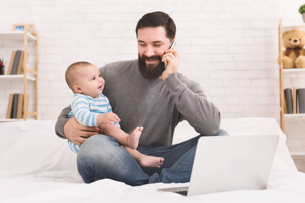 Jeune papa travaillant sur ordinateur portable à la maison avec son fils bébé
 - Photo, image