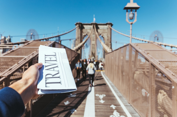 gedeeltelijke weergave van man met reizen krant met wazig zicht van de brug van de new york city op achtergrond - Foto, afbeelding