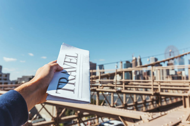 partial view of man holding travel newspaper with blurry new york city bridge view on background - Zdjęcie, obraz