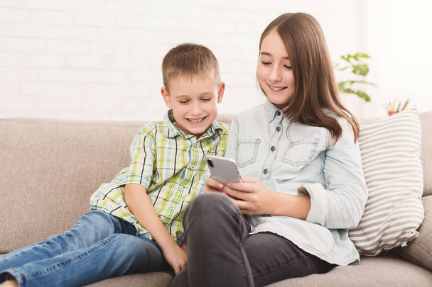 Sister and brother watching cartoons on smartphone together - Valokuva, kuva