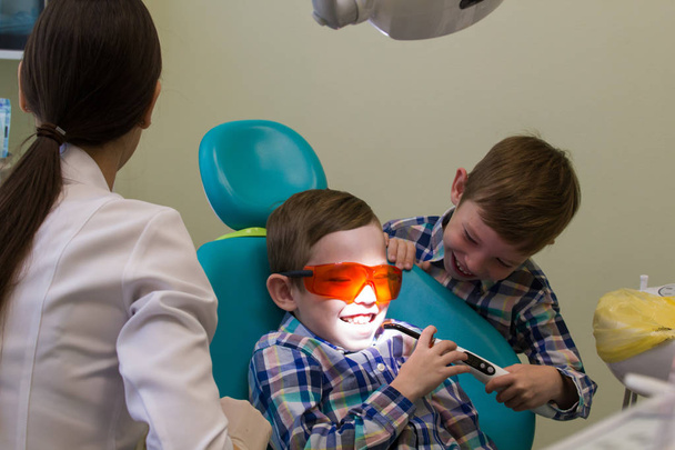 Ontvangst in de tandheelkunde. Een kleine jongen legt op de Bank met bril op, zijn broer houden van de lamp - Foto, afbeelding