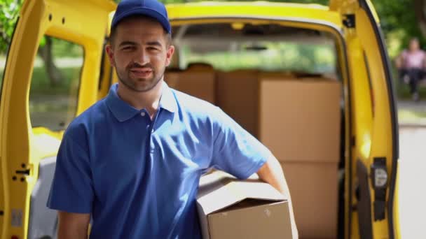 Smiling happy courier man in front of open van doors delivers package and shows ok sign - Imágenes, Vídeo