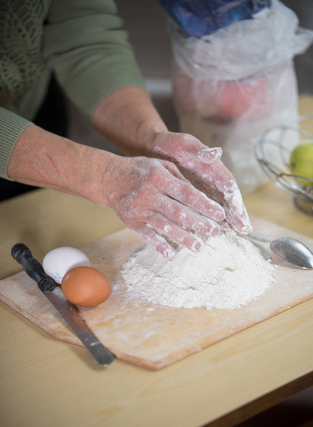 Una anciana haciendo pastelitos. Amasar la masa sobre el escritorio
 - Foto, imagen