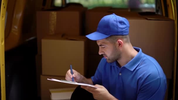 Delivery man is sitting at the back of yellow truck, filling documents - Imágenes, Vídeo