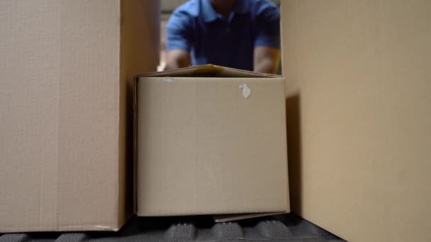 Courier in blue uniform loads boxes into car. Shot from inside of a car - Felvétel, videó