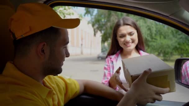 Friendly male deliverer gives parcel to woman while sitting in car - Materiał filmowy, wideo