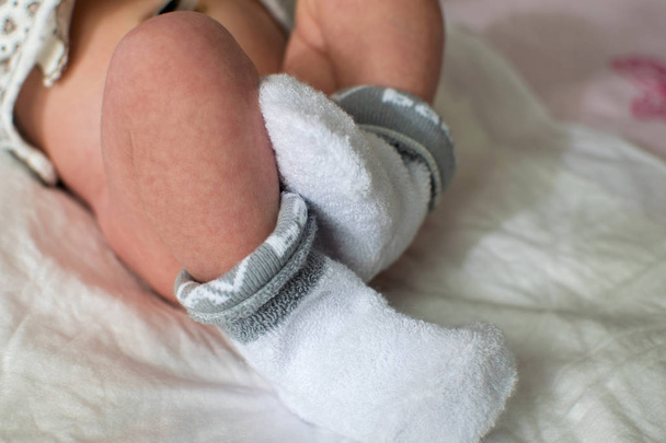Newborn baby feet close up. Baby feet in white terry socks, baby lying on bed, baby's legs. - Foto, imagen