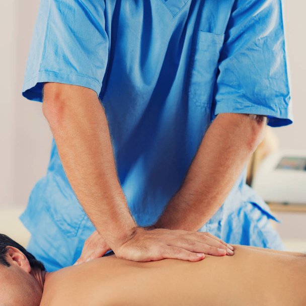 Физиотерапевт лечит спину человека. Терапевт в синей форме. Остеопатия. Регулировка хиропрактики, пациент лежит на массажном столе
 - Фото, изображение