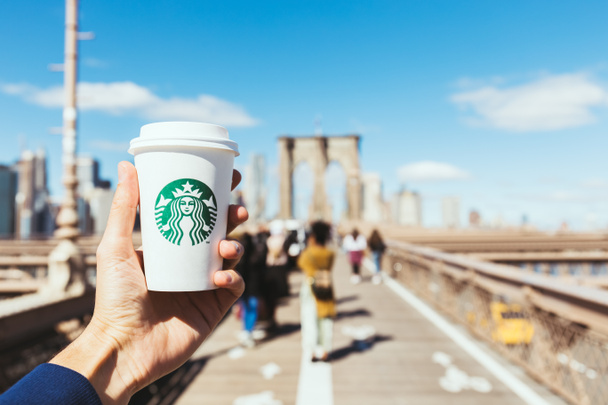NEW YORK, USA - OCTOBER 8, 2018: partial view of man holding starbucks disposable cup of coffee on brooklyn bridge, new york, usa - Photo, image