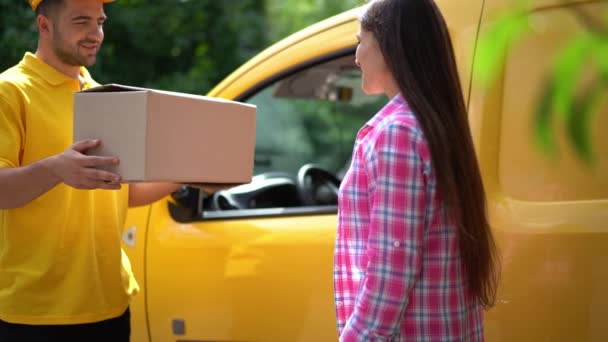 Delivery guy in yellow uniform gives parcel to female customer near car - Záběry, video