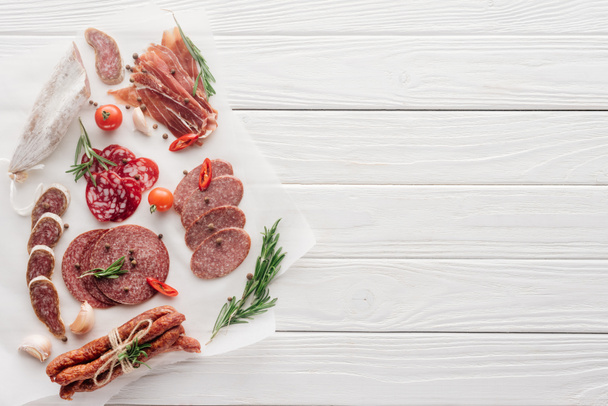 top view of arrangement of various meat snacks and rosemary on white wooden backdrop - Photo, Image