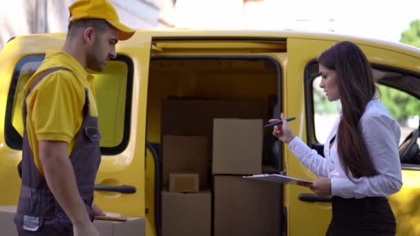 Businesswoman checks delivery from courier in yellow uniform outdoor near his car - Filmati, video