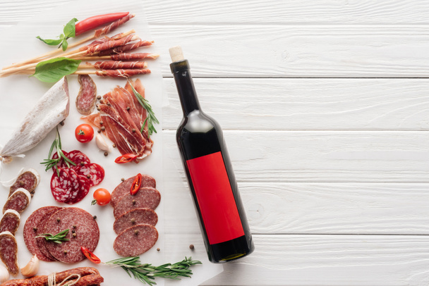 vista superior de la botella de vino tinto y aperitivos variados de carne en la mesa de madera blanca
 - Foto, Imagen