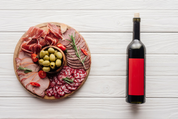pohled shora láhev červeného vína a různé maso občerstvení na bílé dřevěné stolní - Fotografie, Obrázek