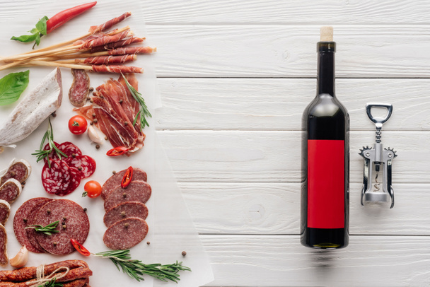 flat lay with bottle of red wine, bottle opener and meat snacks on wooden surface - Foto, Imagem
