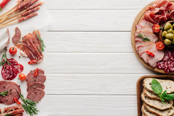 top view of arrangement of various meat snacks and olives on white wooden backdrop - Φωτογραφία, εικόνα