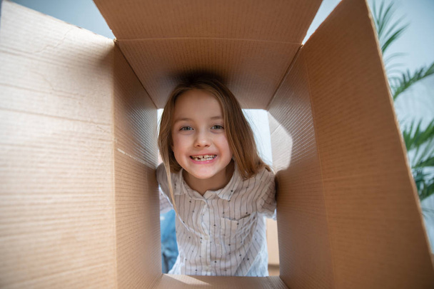 Image of cheerful girl looking out of cardboard box - Фото, зображення