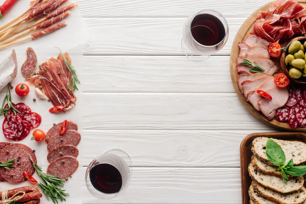 top view of glasses of red wine and delicious meat snacks on white wooden tabletop - Foto, immagini