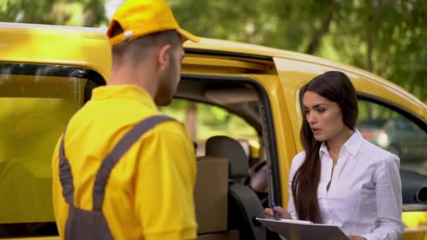 Businesswoman checks delivery from courier in yellow uniform outdoor near his car - Séquence, vidéo