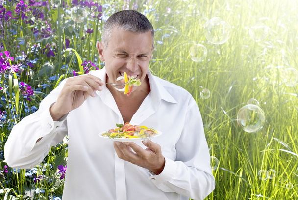 Adult man eating fresh vegetable salad on a summer nature background - Fotó, kép