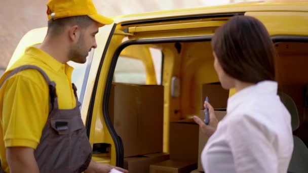 Businesswoman checks delivery from courier in yellow uniform outdoor near his car - Filmati, video