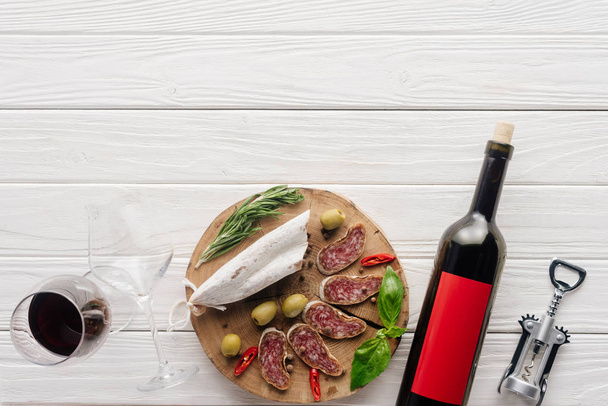 vista dall'alto di bottiglia e bicchiere di vino rosso con antipasti di carne assortiti su superficie in legno bianco
 - Foto, immagini